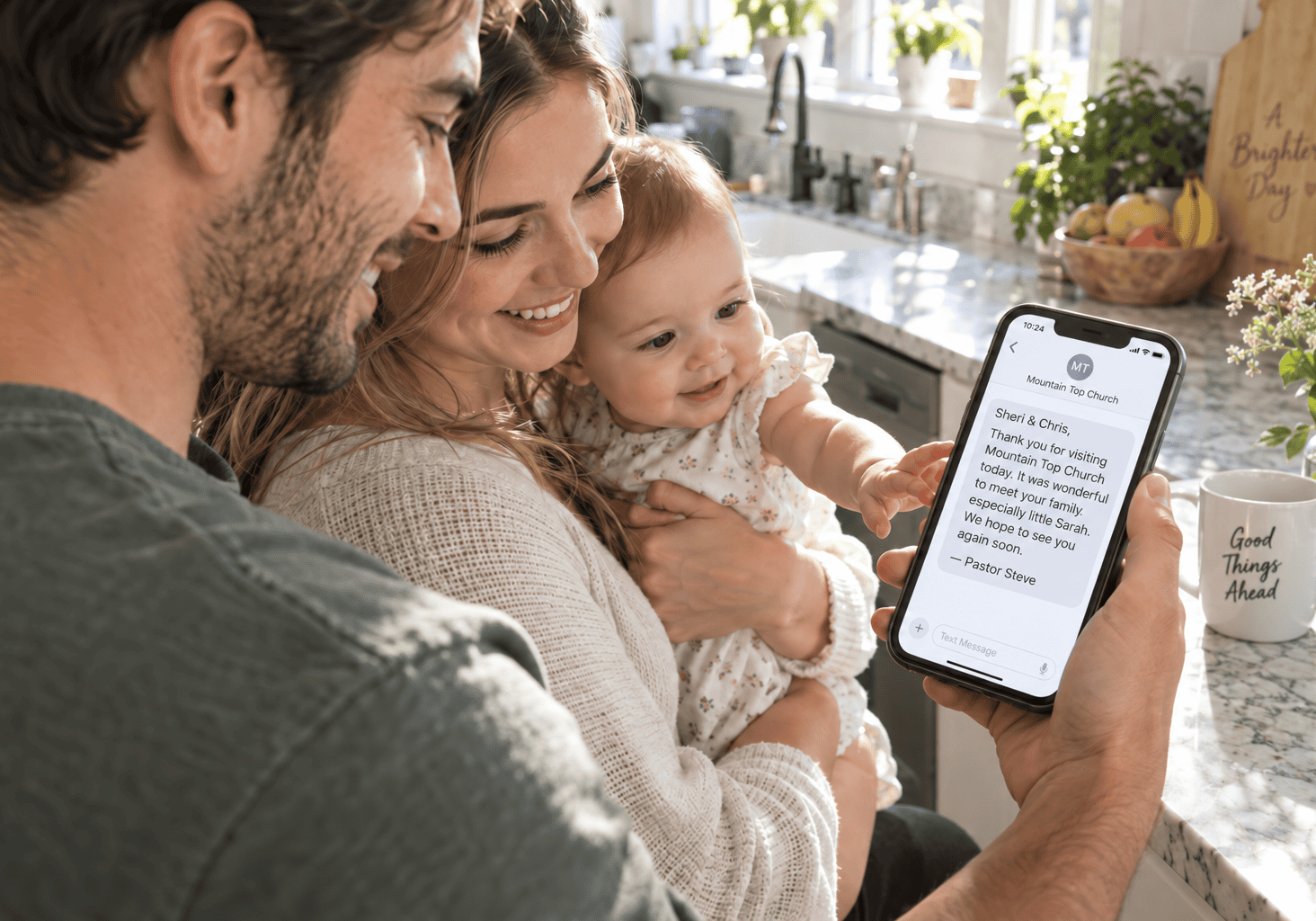 Young parents read Pastor Steve’s personalized thank-you text from Mountain Top Church while their baby reaches for the phone in a sunny kitchen.